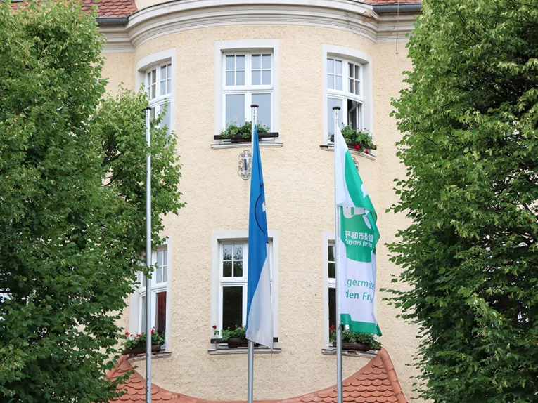 Flaggen wehen vor einem Geb&auml;ude in Atern (Th&uuml;ringen) im Wind. Im Hintergrund ein gelbes Geb&auml;ude.